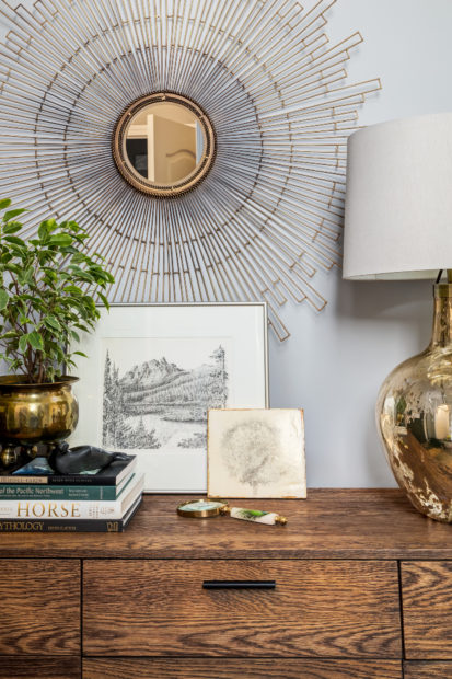 Collection of artifacts and art on a mid century console chest with a gold stardust mirror and a reflective gold lamp.